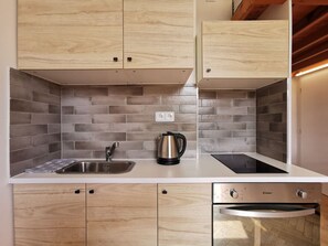 A modern kitchen with wooden cabinets, a stainless steel sink, a kettle, and a built-in oven. - Modern studio with excellent transport links (Praha 10)