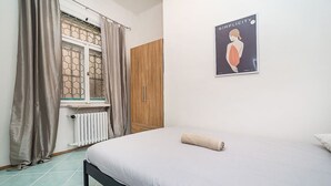 Ein Schlafzimmer mit Bett, Heizkörper, Holzschrank und einem Fenster mit Vorhängen.