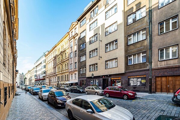 A street lined with parked cars and multi-story buildings with various storefronts.