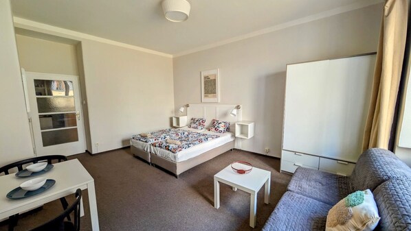 A hotel room with a bed, a small table, a sofa, a desk with chairs, and a wardrobe.