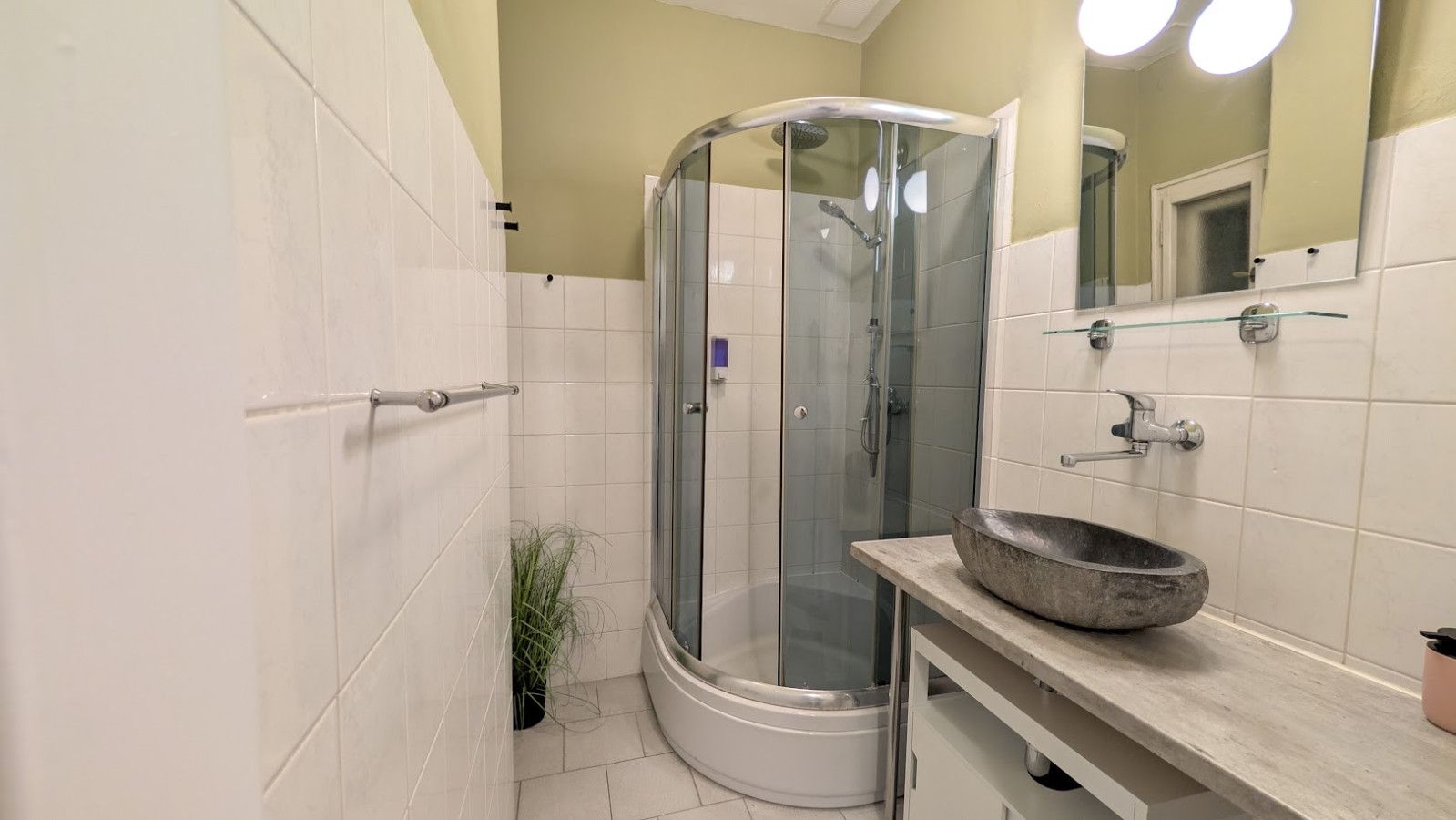A modern bathroom with a glass-enclosed shower, a stone basin sink, and a small potted plant.