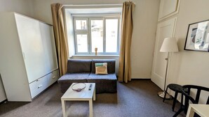 Pieni huone, jossa on sohva, pieni pöytä, lamppu ja ikkuna, jossa on verhot.