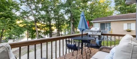 A deck with wicker furniture, a grill, and a view of trees.