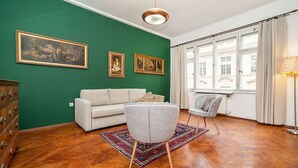 A room with a green wall, a white sofa, a grey armchair, a patterned rug, and a wooden floor. - Classic Old town stay (Praha 1)
