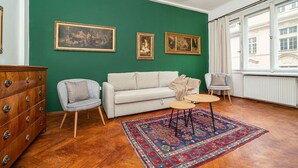 A room with a green wall, a white sofa, a wooden dresser, and a patterned rug. - Classic Old town stay (Praha 1)