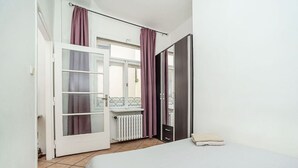 A bedroom with a bed, a radiator, a window with curtains, and a door leading to an outdoor balcony. - Classic Old town stay (Praha 1)