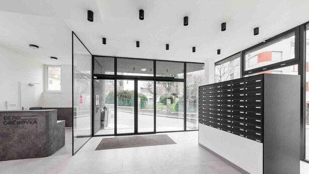 Et moderne receptionsområde med en glasdør, en receptionsdisk og et vægmonteret opbevaringsskab.