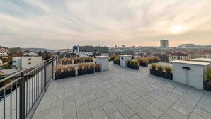 En tagterrasse med udsigt over byen, med flisegulv og plantekasser med grønne planter.