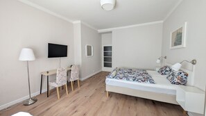 Um quarto moderno com uma cama, uma escrivaninha, cadeiras, uma televisão e um abajur.