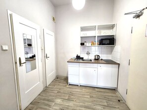 A compact kitchen with white cabinets, a wooden countertop, and a microwave.