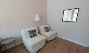 A room with two white armchairs, a small round table, a floor lamp, and a mirror on the wall.