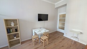 A room with a white table and chairs, a bookshelf, a TV mounted on the wall, and a small white table against the wall.