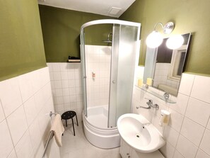 A bathroom with a glass-enclosed shower, a white sink, and a mirror with lights.