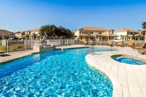Une piscine avec une terrasse, entourée de maisons et d’une clôture.
