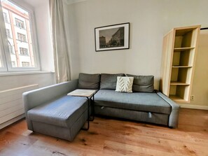 A modern living room with a grey sectional sofa, a small ottoman, a framed picture on the wall, and a wooden floor.