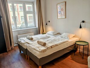A bedroom with a bed, bedside lamps, a small table, and a window with curtains.