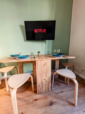 A dining area with a wooden table, four chairs, and a television mounted on the wall displaying "NETFLIX".