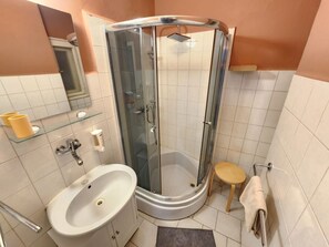 A bathroom with a glass-enclosed shower, a sink, a toilet, and a small wooden stool.