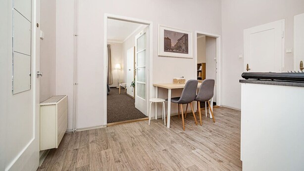 A modern kitchen with white cabinets, a dining area with a table and chairs, and a hallway leading to another room.