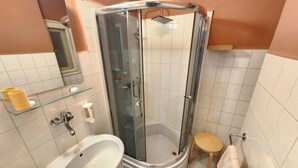 A bathroom with a glass-enclosed shower, a sink, a toilet, and a small wooden stool.