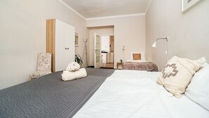 A bedroom with two beds, a bedside table, a lamp, and a door leading to a bathroom.