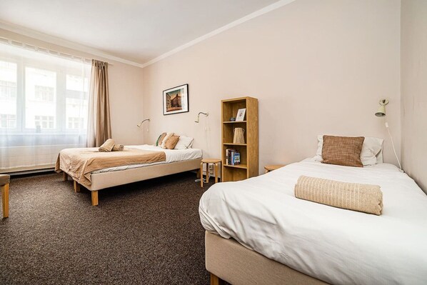 A hotel room with two beds, a bookshelf, a picture on the wall, and a window with curtains.