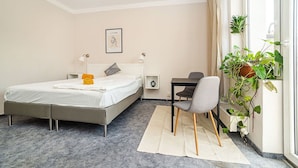Quarto com cama, mesa de cabeceira, cadeira e um vaso de planta perto da janela.