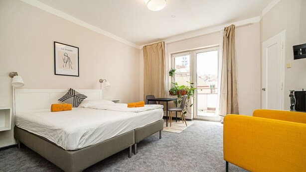 Quarto de hotel com cama, escrivaninha, cadeira e varanda com cortinas.