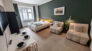 A bedroom with a bed, two chairs, a desk with a computer, and a window.