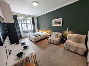 A bedroom with a bed, two chairs, a desk with a computer, and a window.