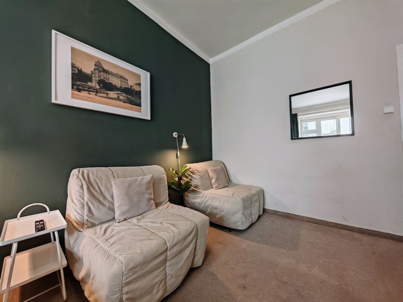 A room with two beige sofas, a small table with a tray, a framed picture on the wall, and a floor lamp.