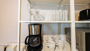 A kitchen with a coffee maker, mugs, and glassware on shelves.