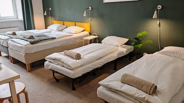 A hotel room with three single beds, a small table, and a chair.