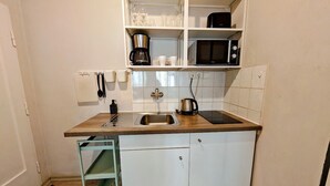 A compact kitchen with a sink, a coffee maker, a microwave, and a cabinet with glassware.