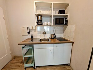 A compact kitchen with a sink, a coffee maker, a microwave, and a cabinet with glassware.