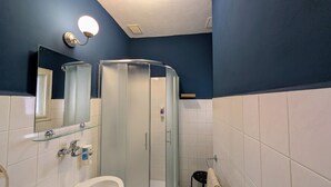 A bathroom with a glass shower enclosure, a toilet, a sink with a glass shelf, and a mirror.
