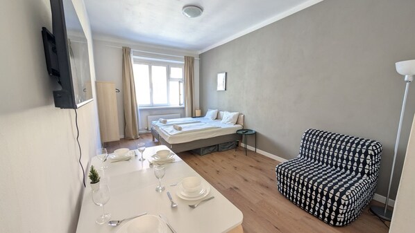 A hotel room with a bed, a dining table set with plates and glasses, a patterned armchair, and a small plant. - Comfortable apartment sleeps 6 (Praha 3)