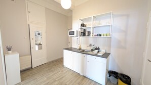 A compact kitchen with a microwave, coffee maker, and a sink. There is a white cabinet with a countertop, and a small trash bin is visible.