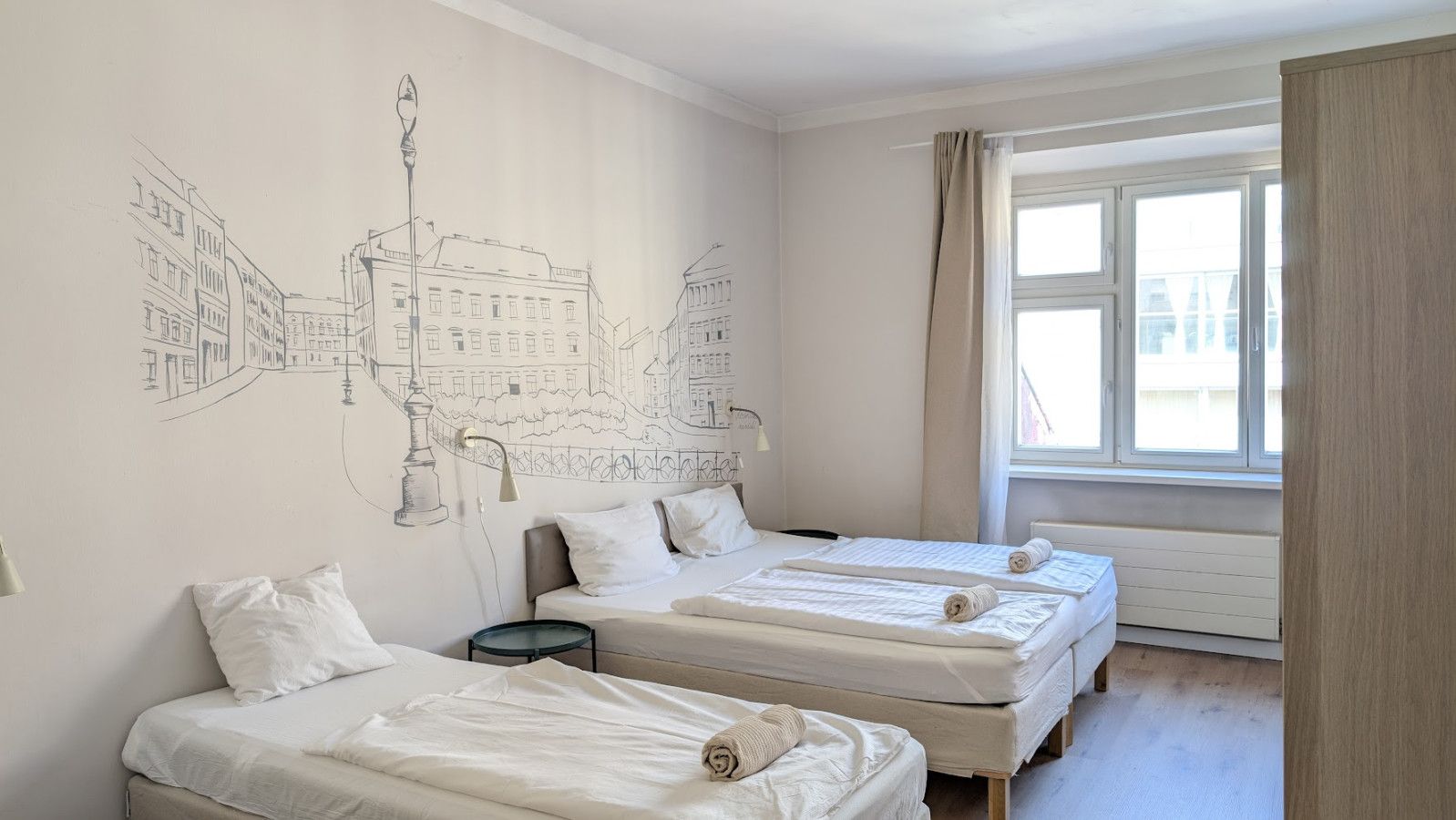 A bedroom with two beds, a wall mural, a window with curtains, and a radiator.