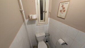 A small, narrow bathroom with a toilet, a window, and a framed picture on the wall. - Comfortable apartment sleeps 6 (Praha 3)