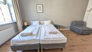 A double bed with white linens, a small bedside table, a chair with a checkered pattern, and a framed artwork on the wall. - Comfortable apartment sleeps 6 (Praha 3)