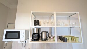 A kitchenette with a microwave, coffee maker, and tea kettle on white shelves.