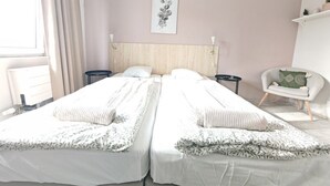A bedroom with two beds, a bedside table, a chair, and a wall-mounted artwork.