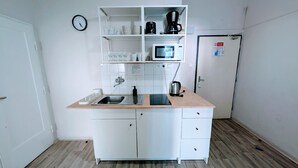 A compact kitchen with a sink, microwave, coffee maker, and shelves with glasses and cups.