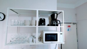 A kitchen with a white shelf unit holding glassware, a coffee maker, and a microwave.