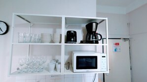 A kitchen with a white shelf unit holding glassware, a coffee maker, and a microwave.