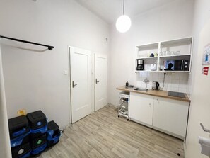 A compact kitchen with white cabinets, a wooden countertop, a microwave, a coffee maker, and a small sink. There are two white doors and a ceiling light.