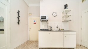 A compact kitchen with white cabinets, a microwave, a kettle, and a clock on the wall. - Comfortable apartment sleeps 8 (Praha 3)