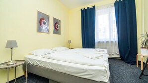 A hotel room with a bed, two bedside tables, a lamp, a potted plant, and a window with curtains. - Comfortable apartment sleeps 8 (Praha 3)