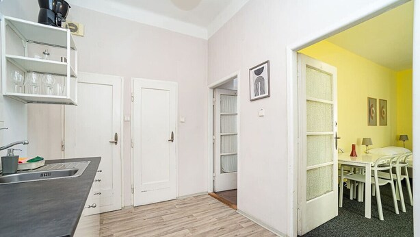 A compact kitchen with a sink, white cabinets, and a wooden floor. There is a dining area with a table and chairs, and a door leading to another room. - Comfortable apartment sleeps 8 (Praha 3)